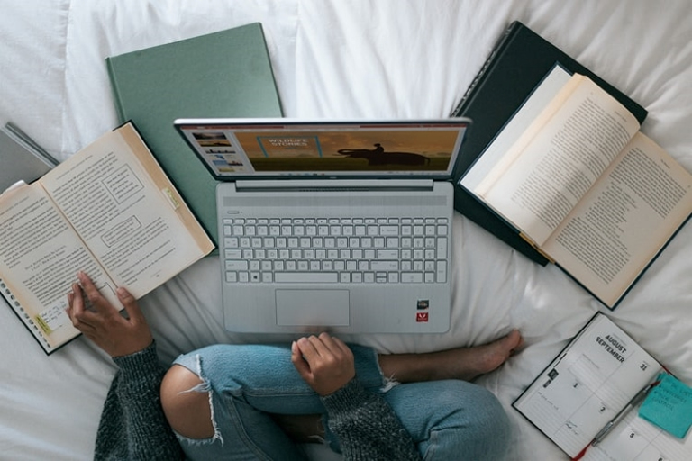 woman sitting on bed woth laptop and books learning italian